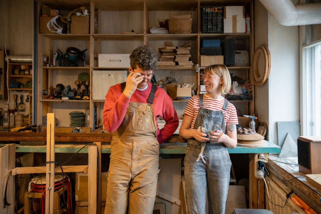 Two people collaborating at a workbench in a woodworking shop, tools and materials in the background.
